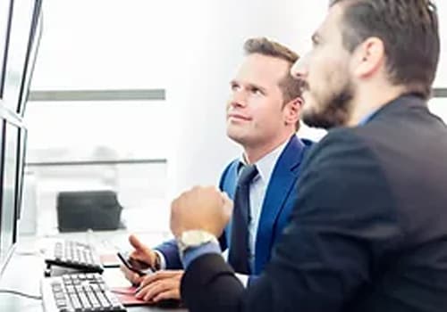 Two people in discussion at a desk with computer screens